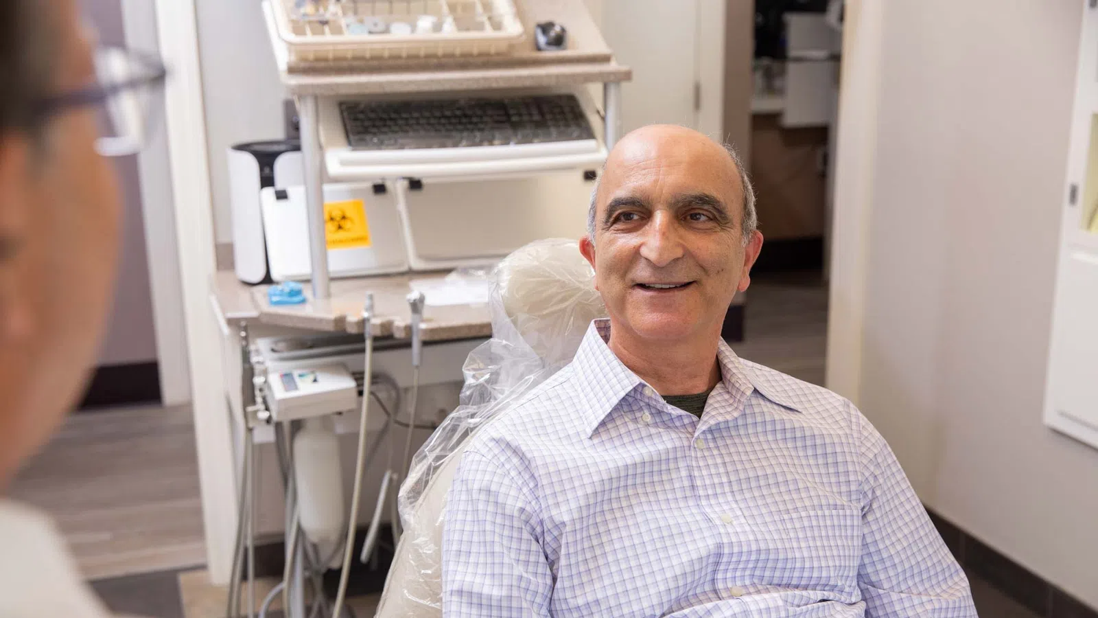 Middle-aged man smiling while sitting in dental chair during consultation with dentist
