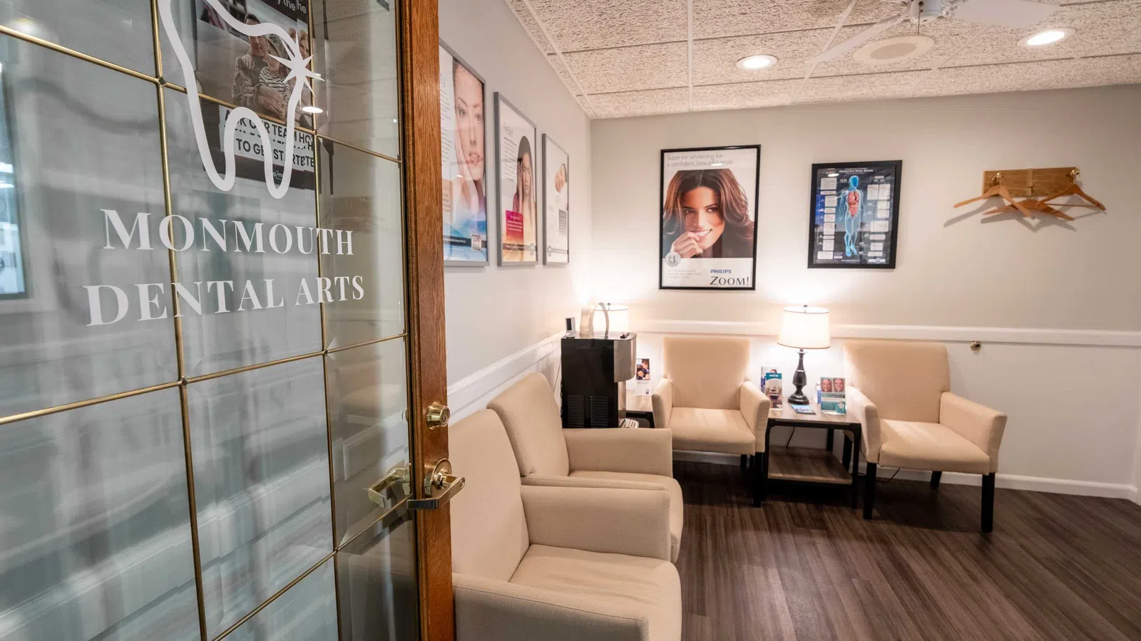 Bright, modern dental office waiting room with beige chairs, wood flooring, and posters on cream walls.
