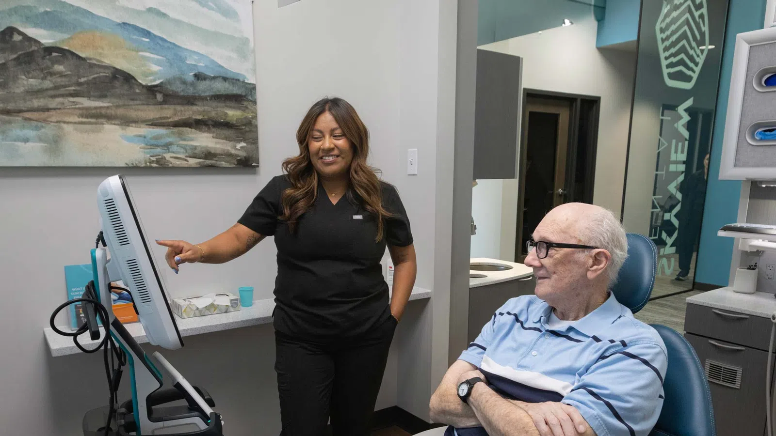 Dental professional reviews information on screen with elderly male patient in modern clinic room.