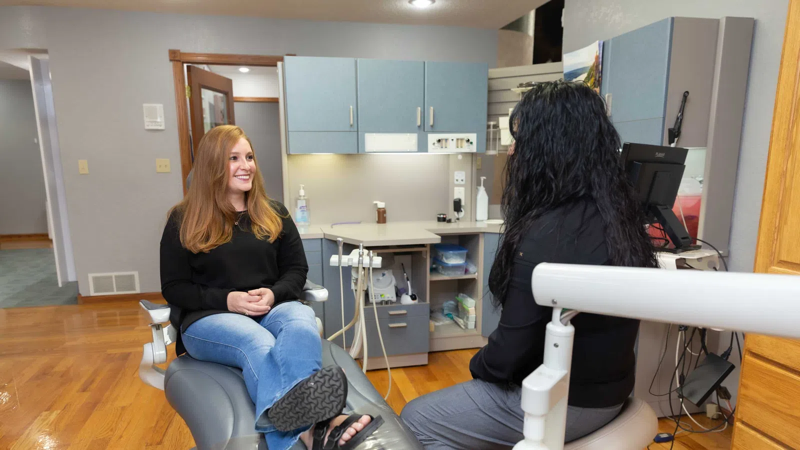 Patient with red hair talks with dental hygienist in a modern dental clinic with blue cabinets and hardwood floor