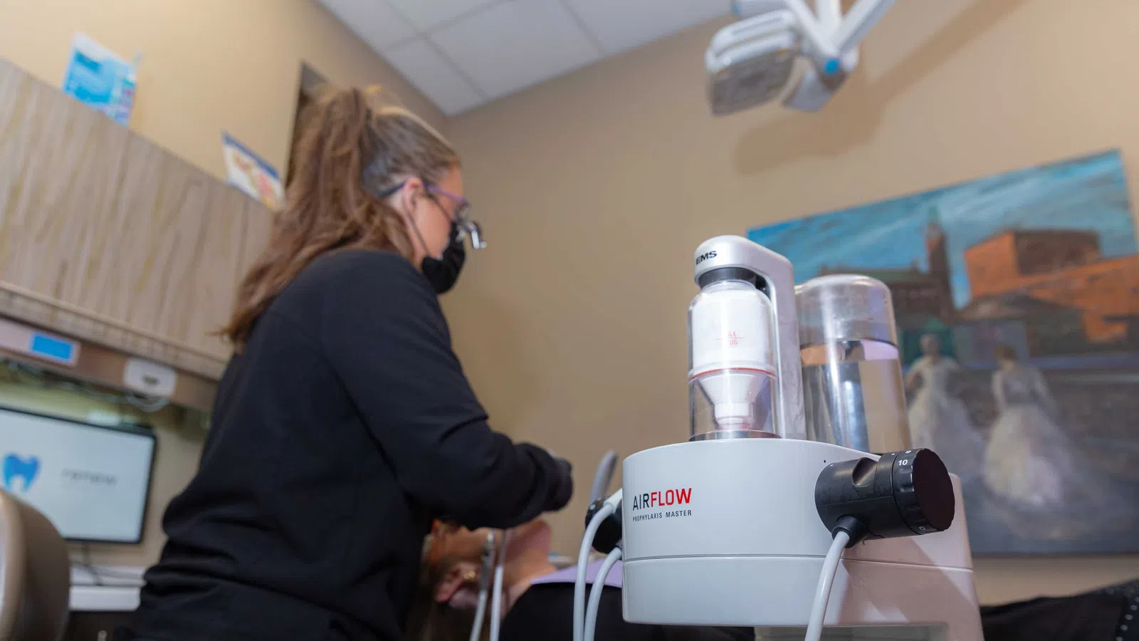 Dental hygienist uses airflow machine for patient teeth cleaning in a modern clinic setting.