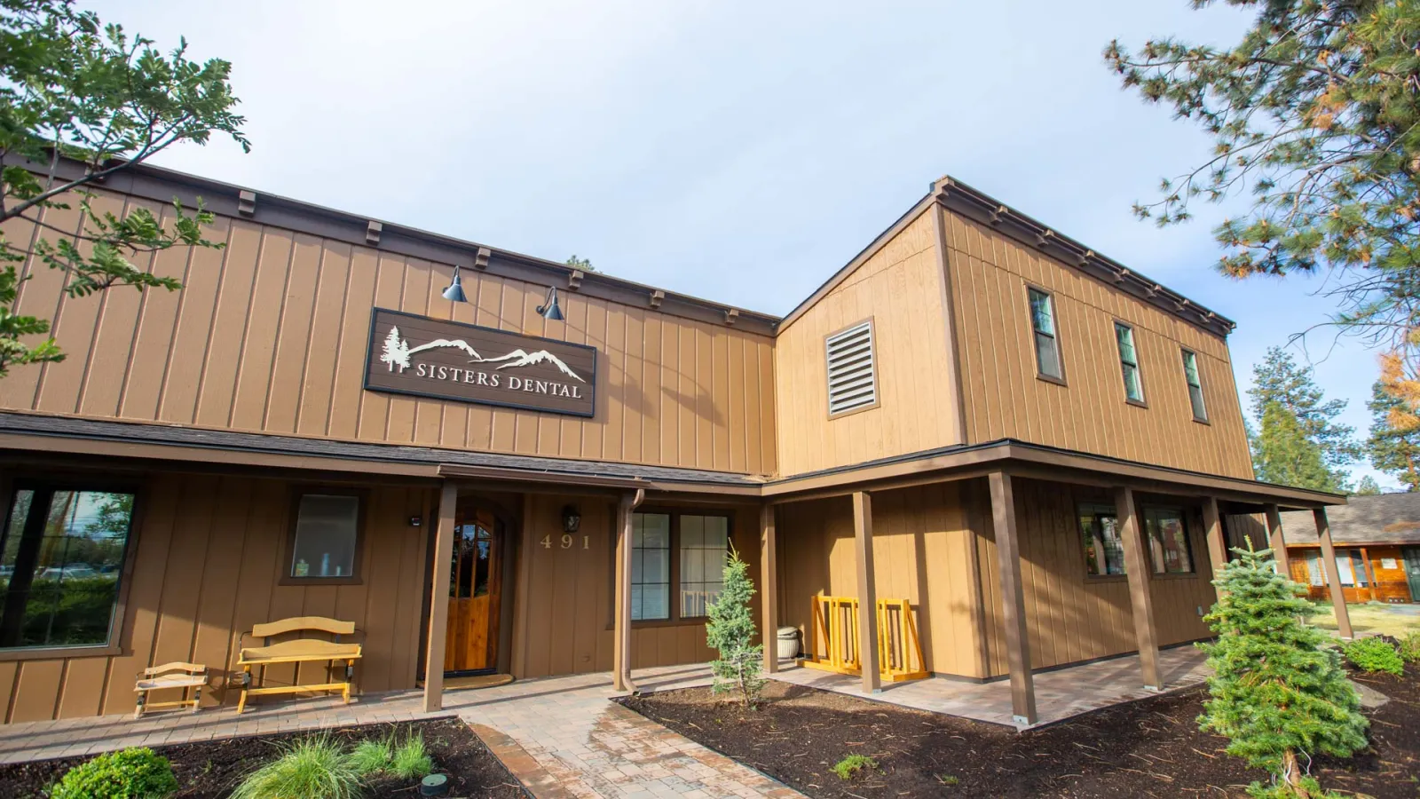 Exterior of Sisters Dental office building with wooden facade and landscaped front yard under clear sky