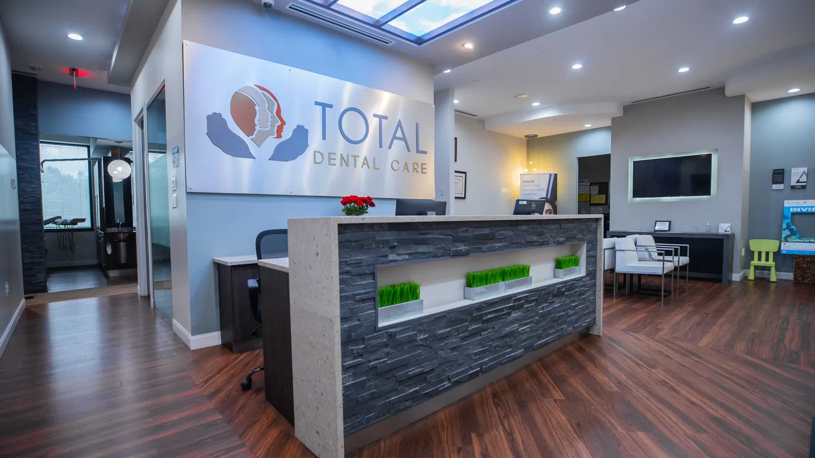 Modern dental office reception area with wood flooring, stone front desk, and Total Dental Care signage.