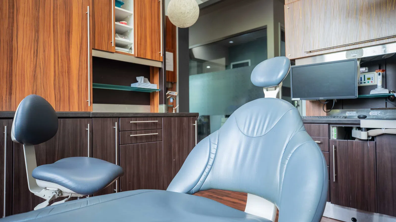 Modern dental clinic interior featuring a blue patient chair, wooden cabinets, and medical equipment.