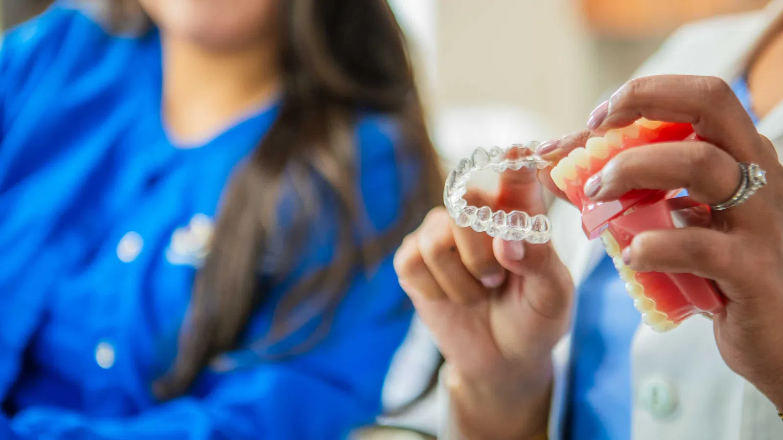 Dentist demonstrating how to use a clear dental aligner on a teeth model during consultation.