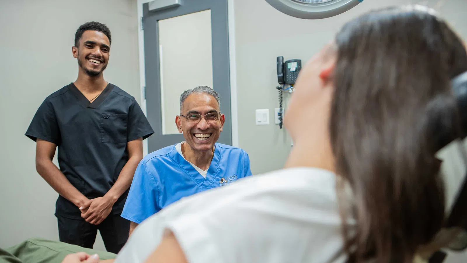 Male doctor and assistant smiling at female patient in medical office during consultation.