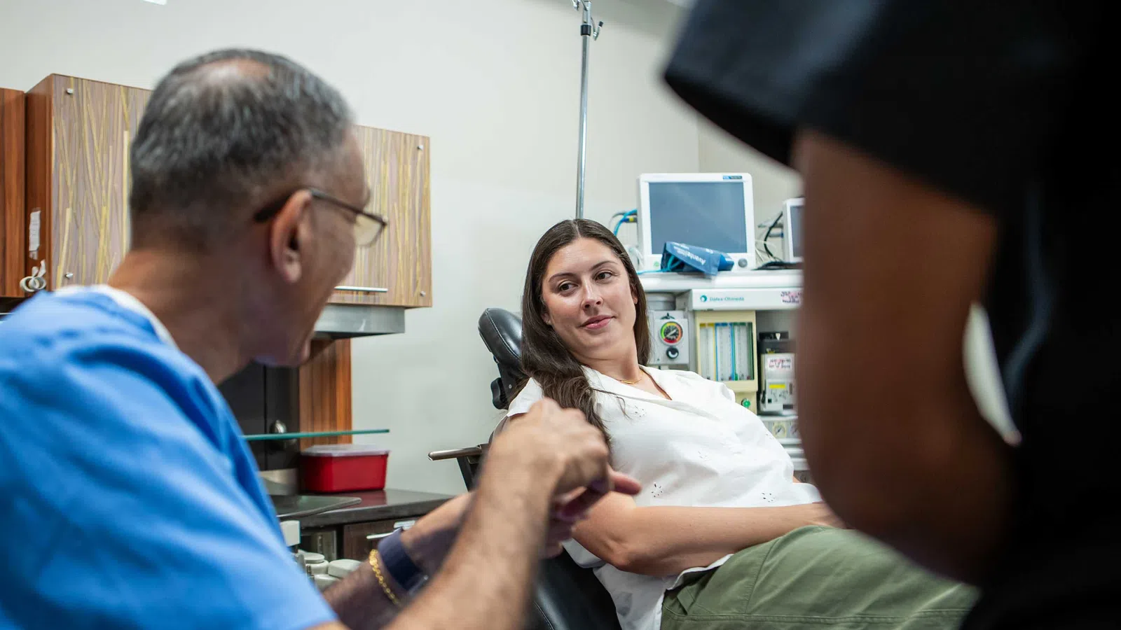 Patient in a medical clinic consulting with a healthcare professional wearing blue scrubs and glasses.