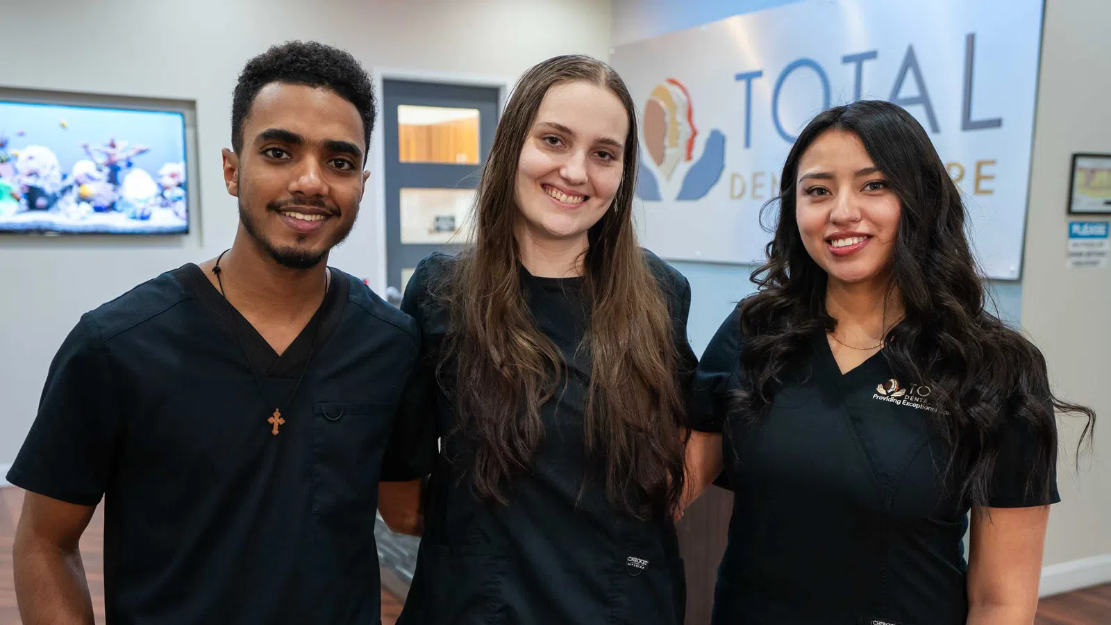 Three dental professionals in black scrubs smiling inside Total Dental Care clinic lobby.