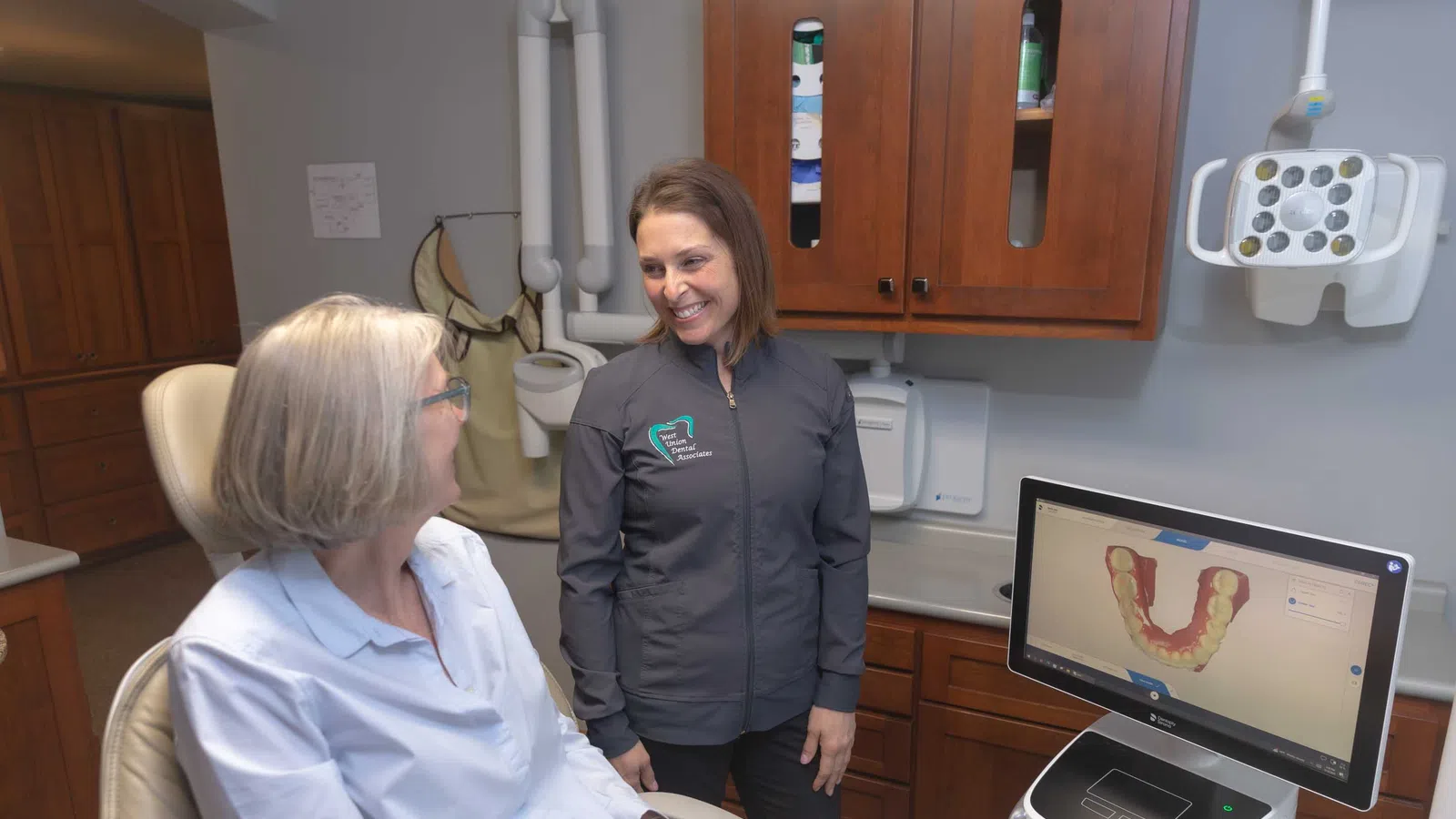 Dentist consulting female patient in a dental office with 3D dental scan shown on monitor.
