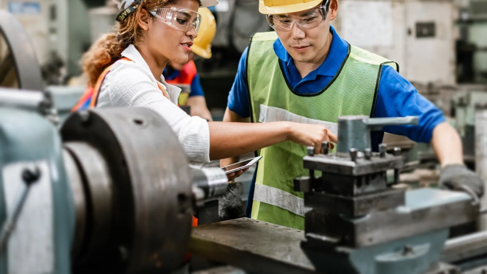 Two factory workers in safety gear operating heavy machinery in an industrial manufacturing setting