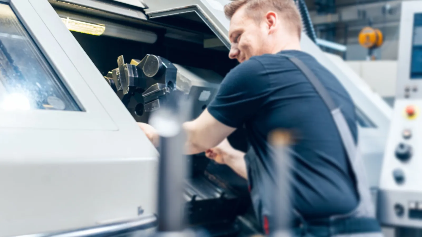 Technician adjusting machinery inside a CNC lathe in a modern industrial workshop environment.