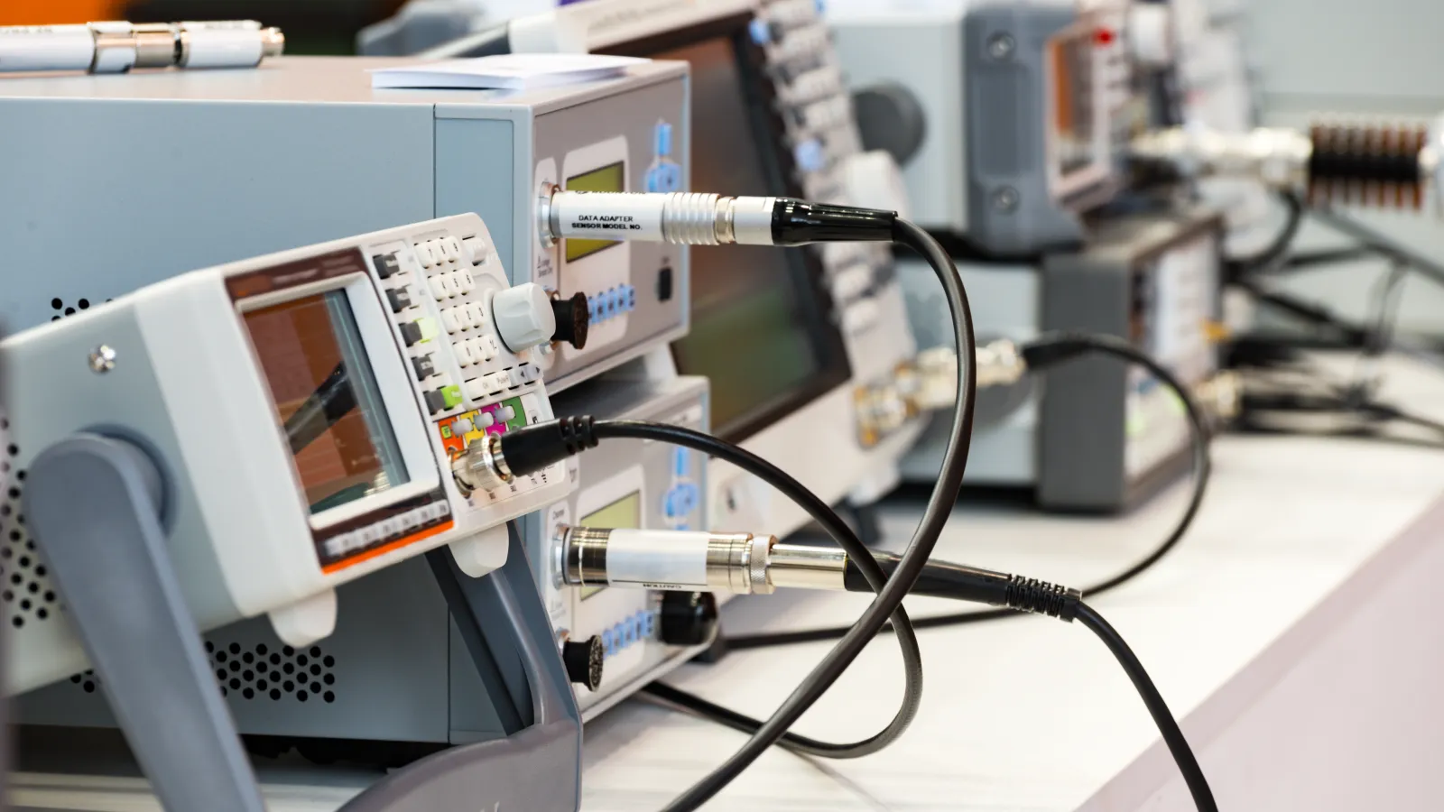 Multiple electronic testing devices with screens and cables connected on a lab bench for measurement and analysis.