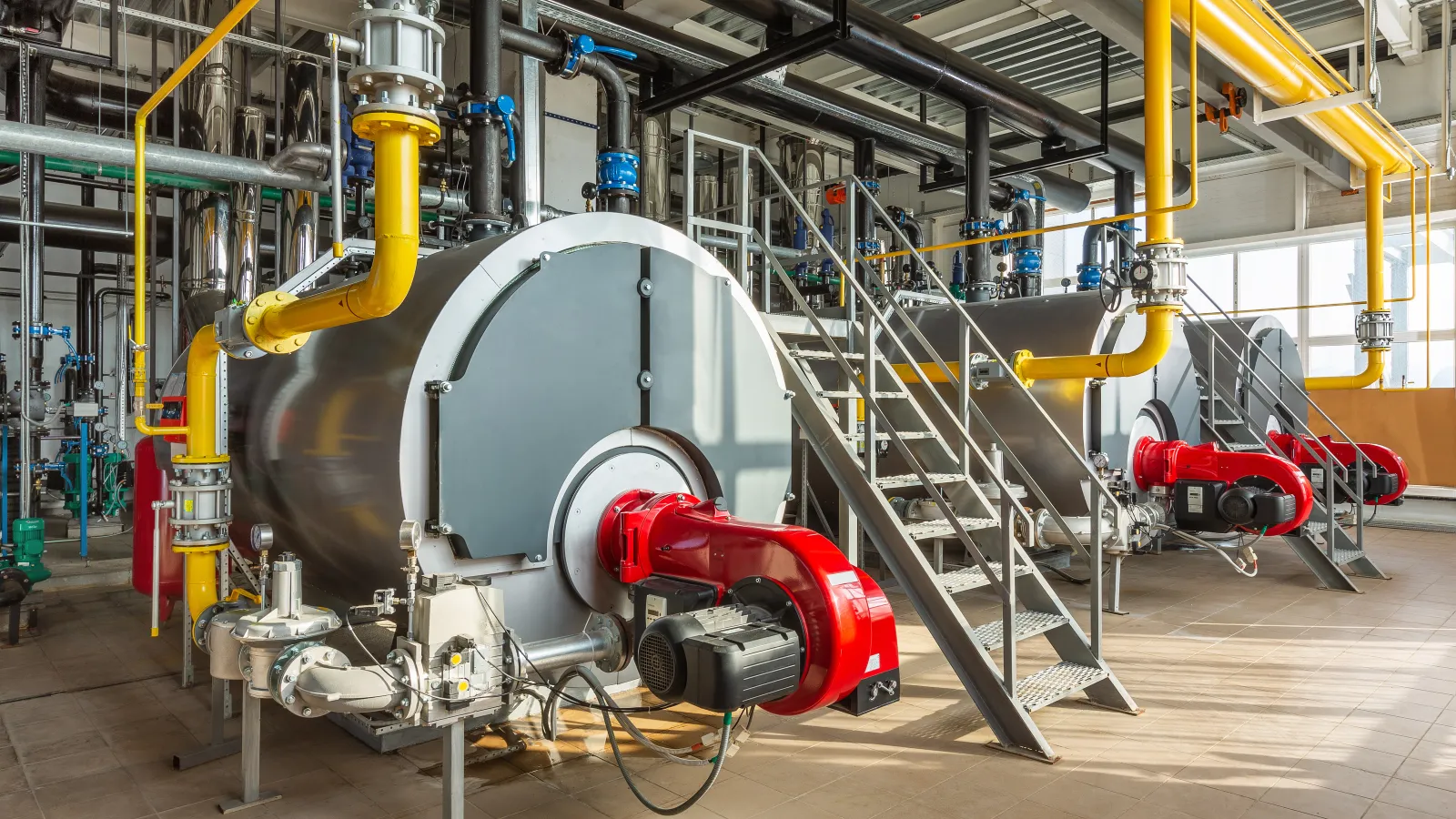 Industrial boilers with red burners and yellow pipelines in a factory boiler room.