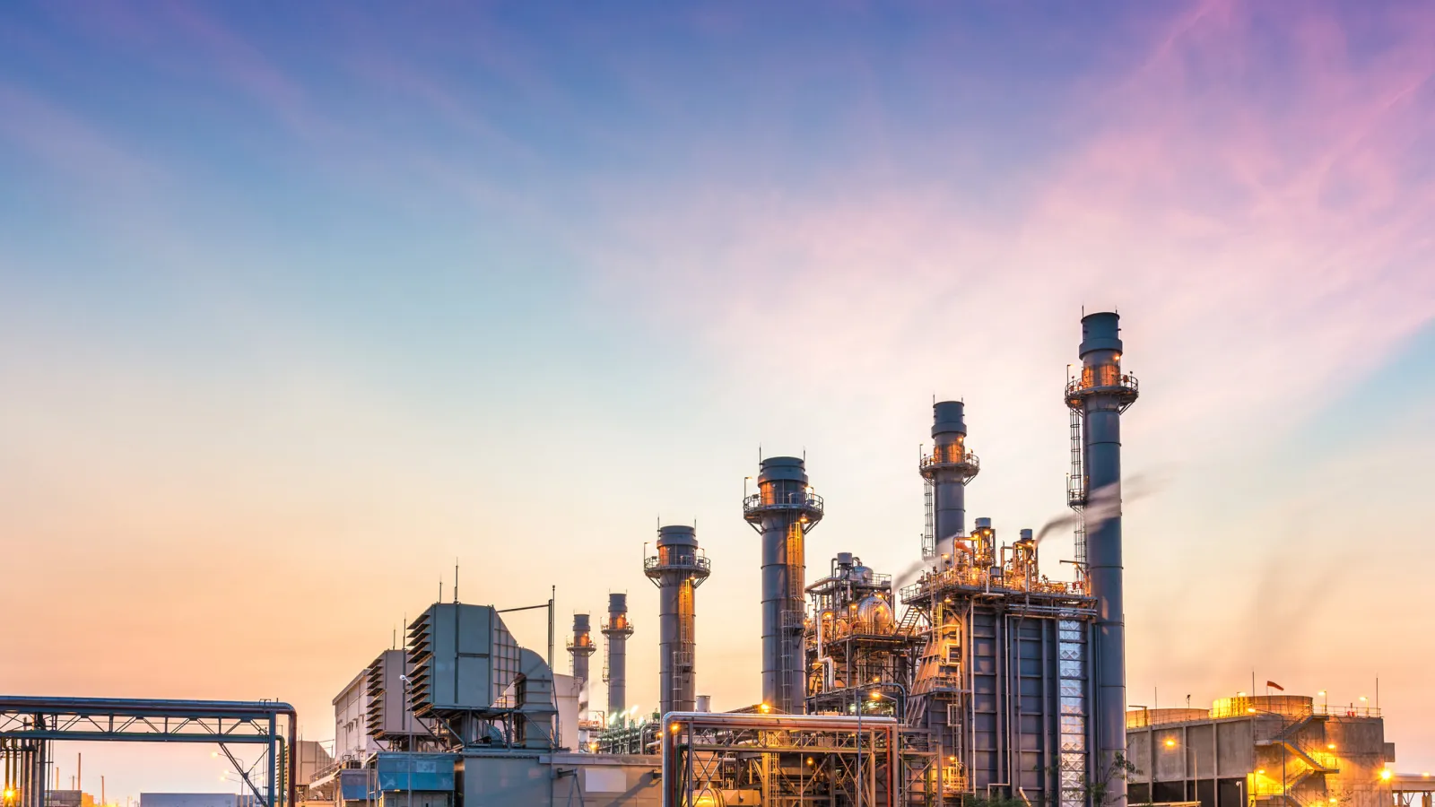 Industrial power plant with tall chimneys and complex structures under a colorful twilight sky.