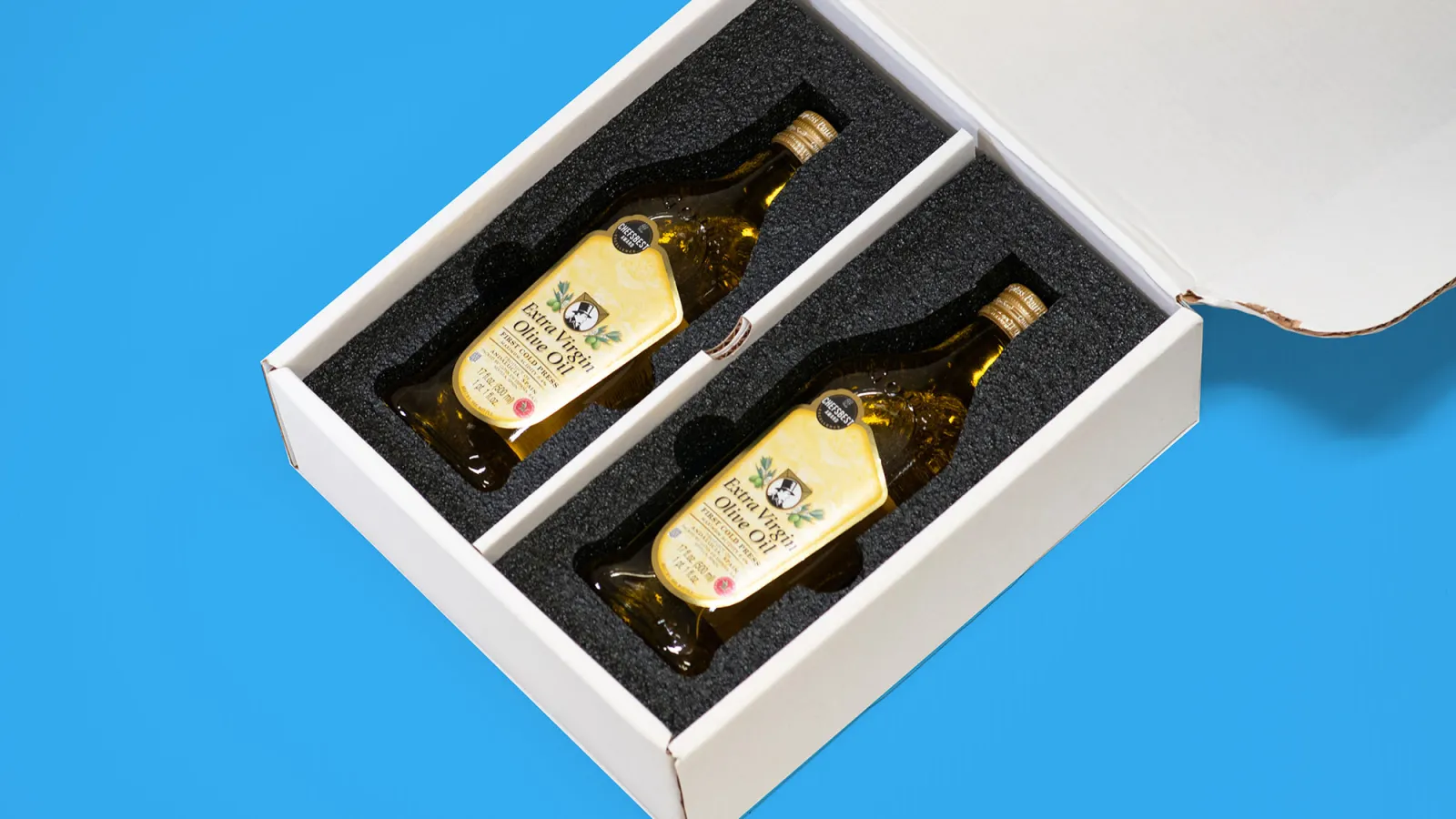 Two bottles of extra virgin olive oil packaged securely in a white box with foam inserts against a blue background