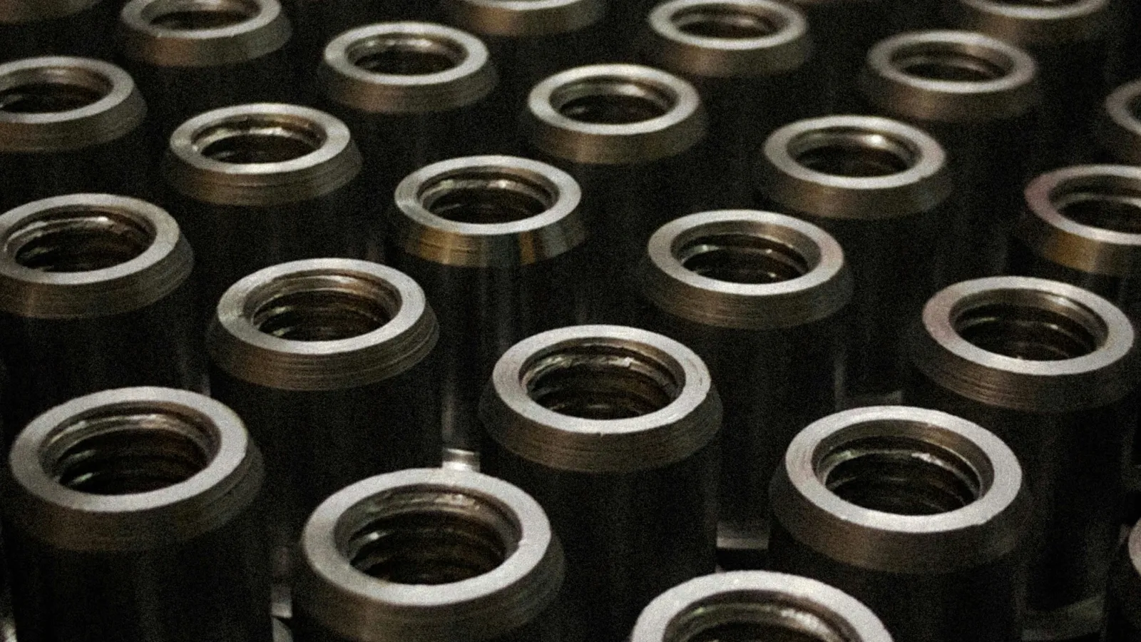 Close-up of numerous threaded metal cylindrical parts arranged in rows inside a factory setting.
