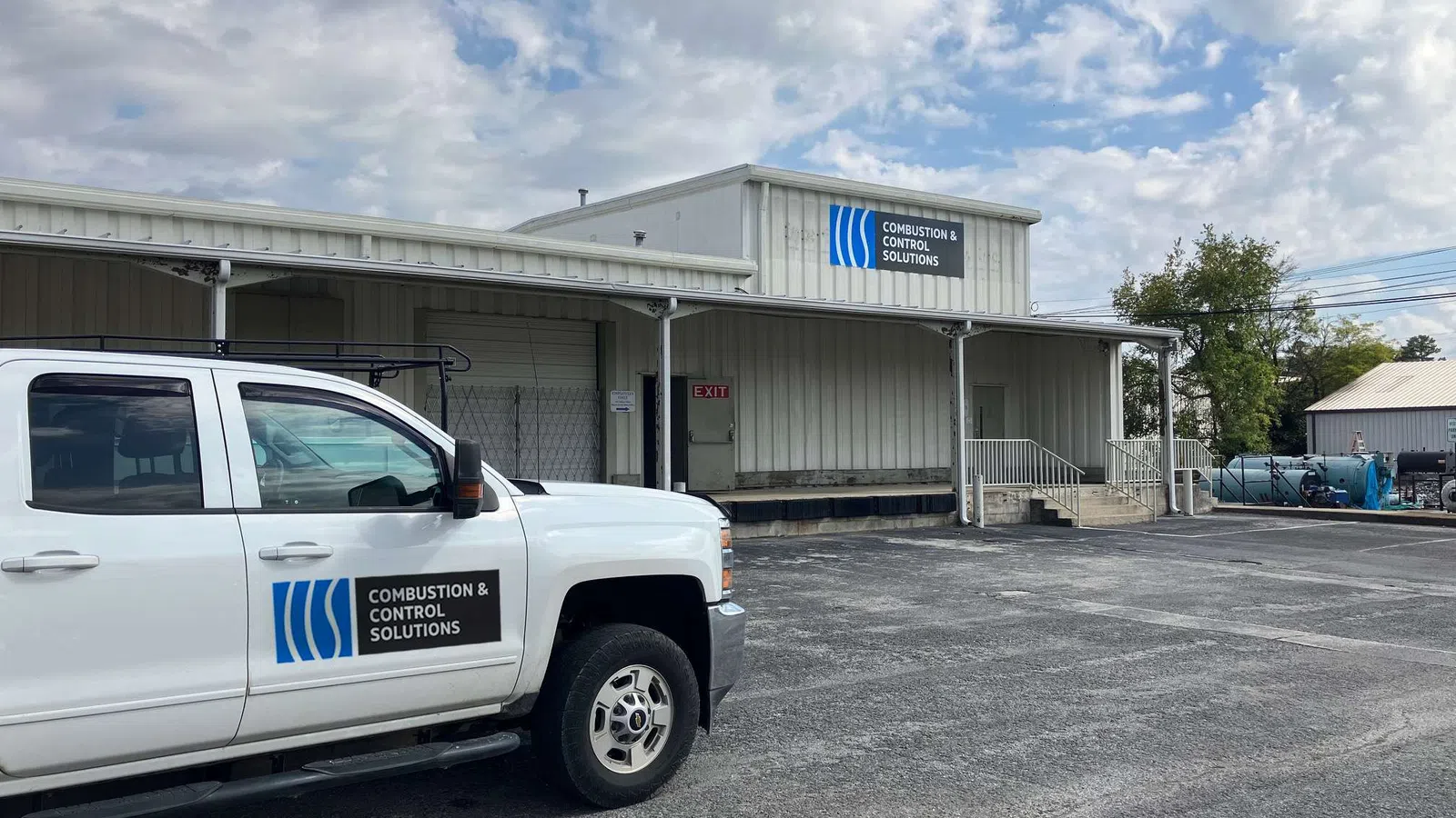 White truck and building with Combustion & Control Solutions signage under partly cloudy sky