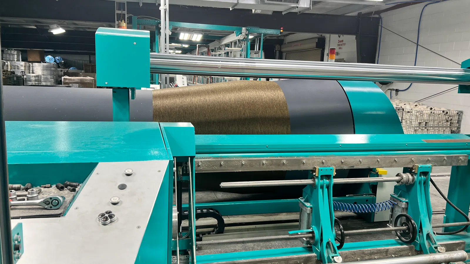 Industrial textile machine winding brown yarn onto a large spool in a factory setting
