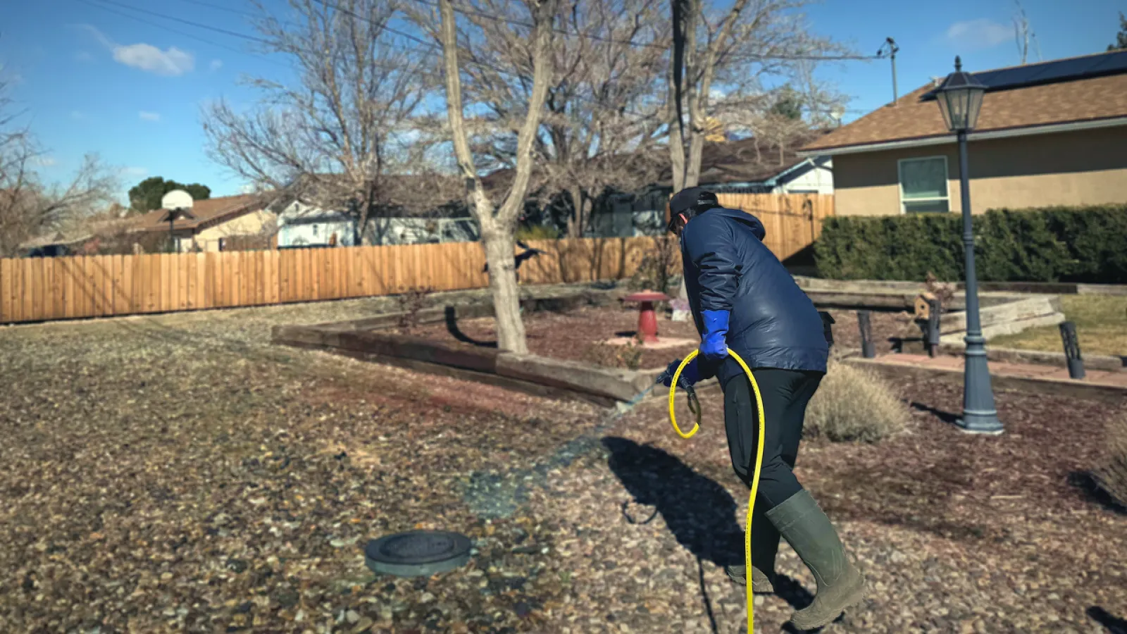 Person in waterproof gear cleaning a yard with a hose on a sunny day.