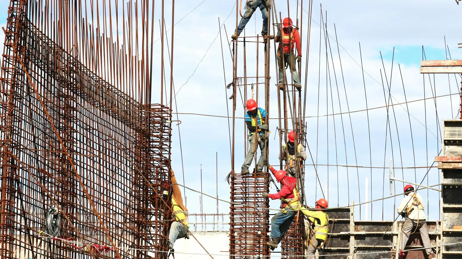 Construction workers wearing safety gear working on steel reinforcement bars at a building site under a clear sky