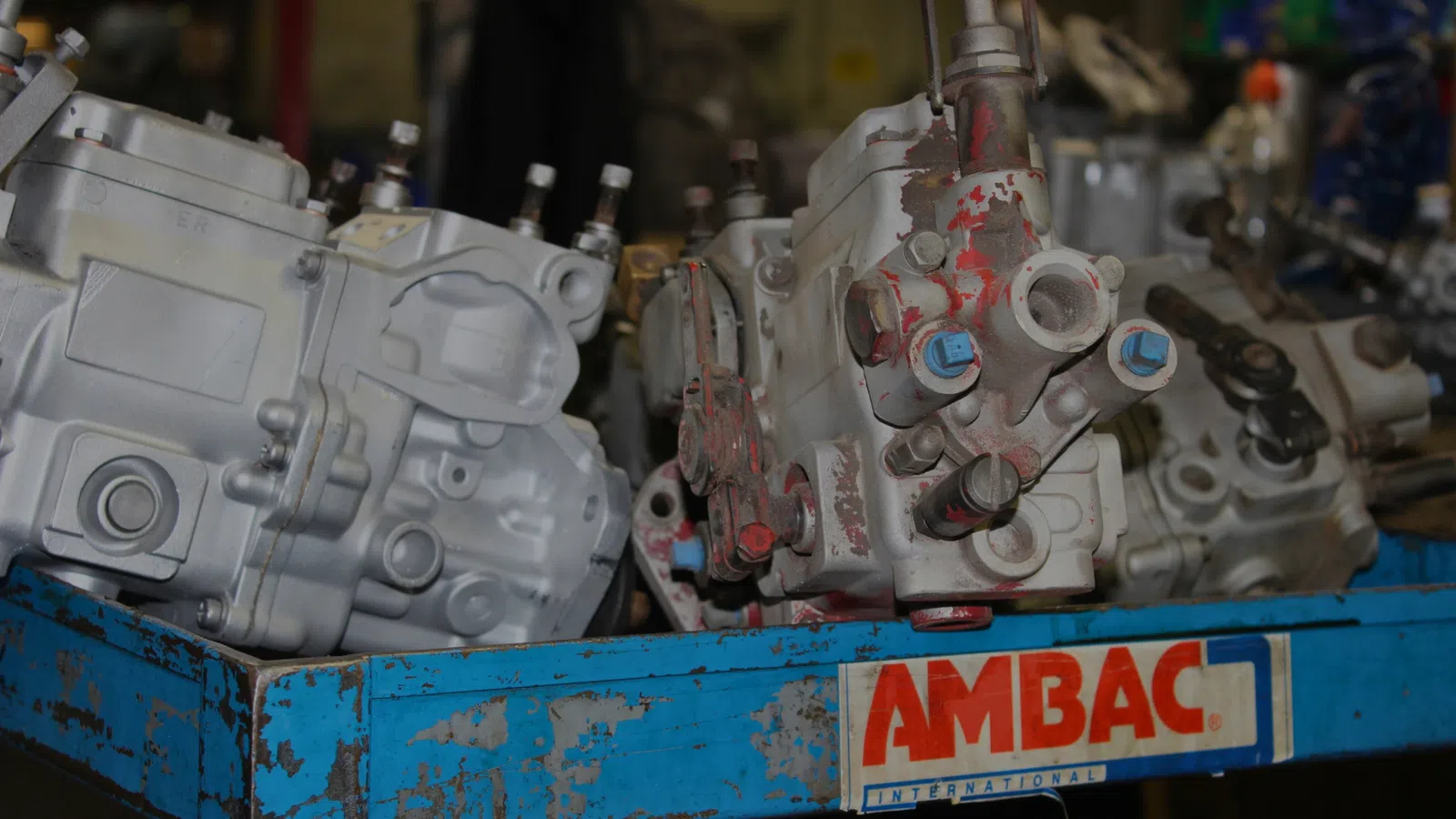 Used mechanical parts with bolts and fittings placed on a blue container with worn AMBAC label