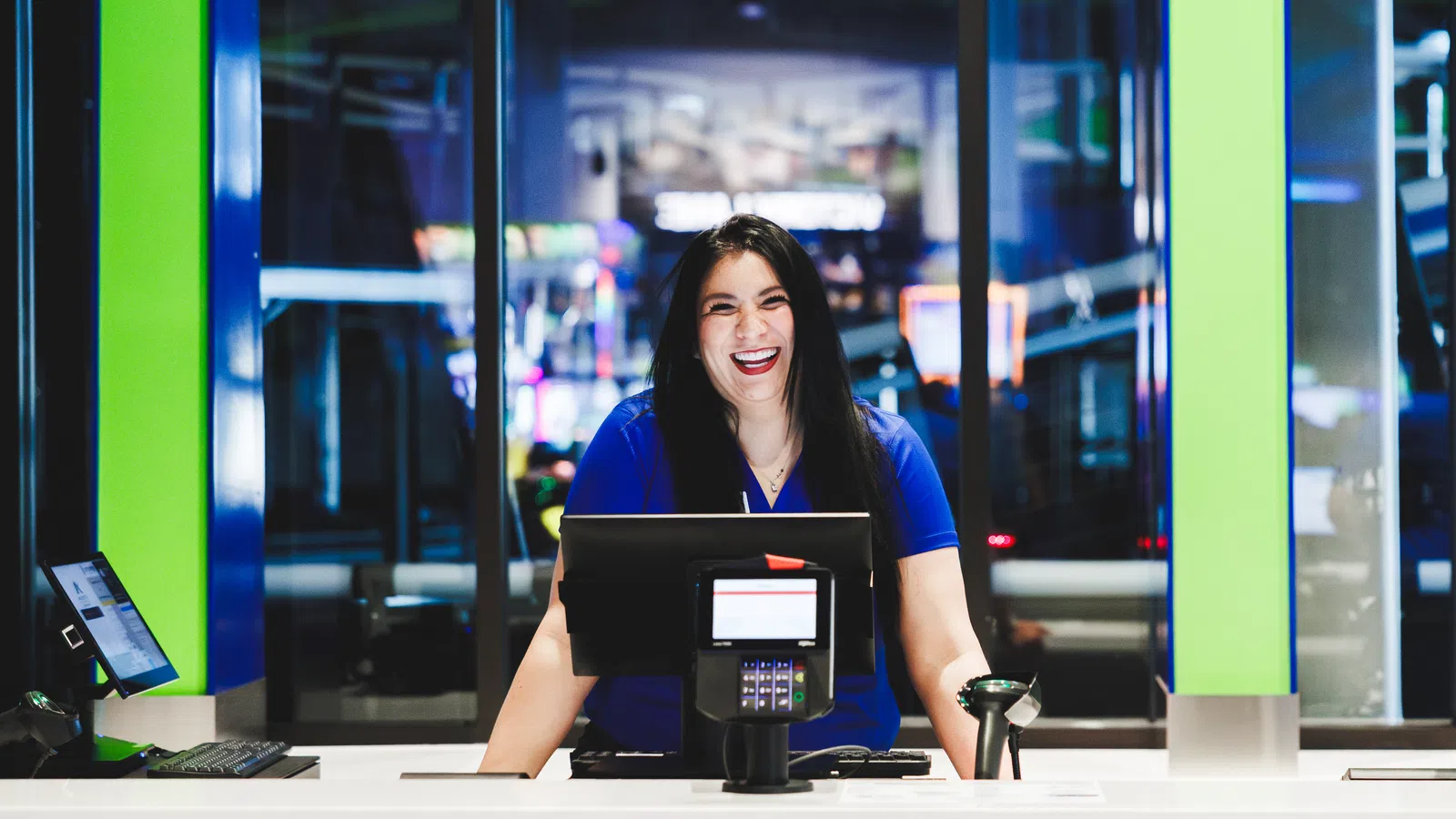 Smiling female cashier standing behind counter with computer and scanner in modern retail store.