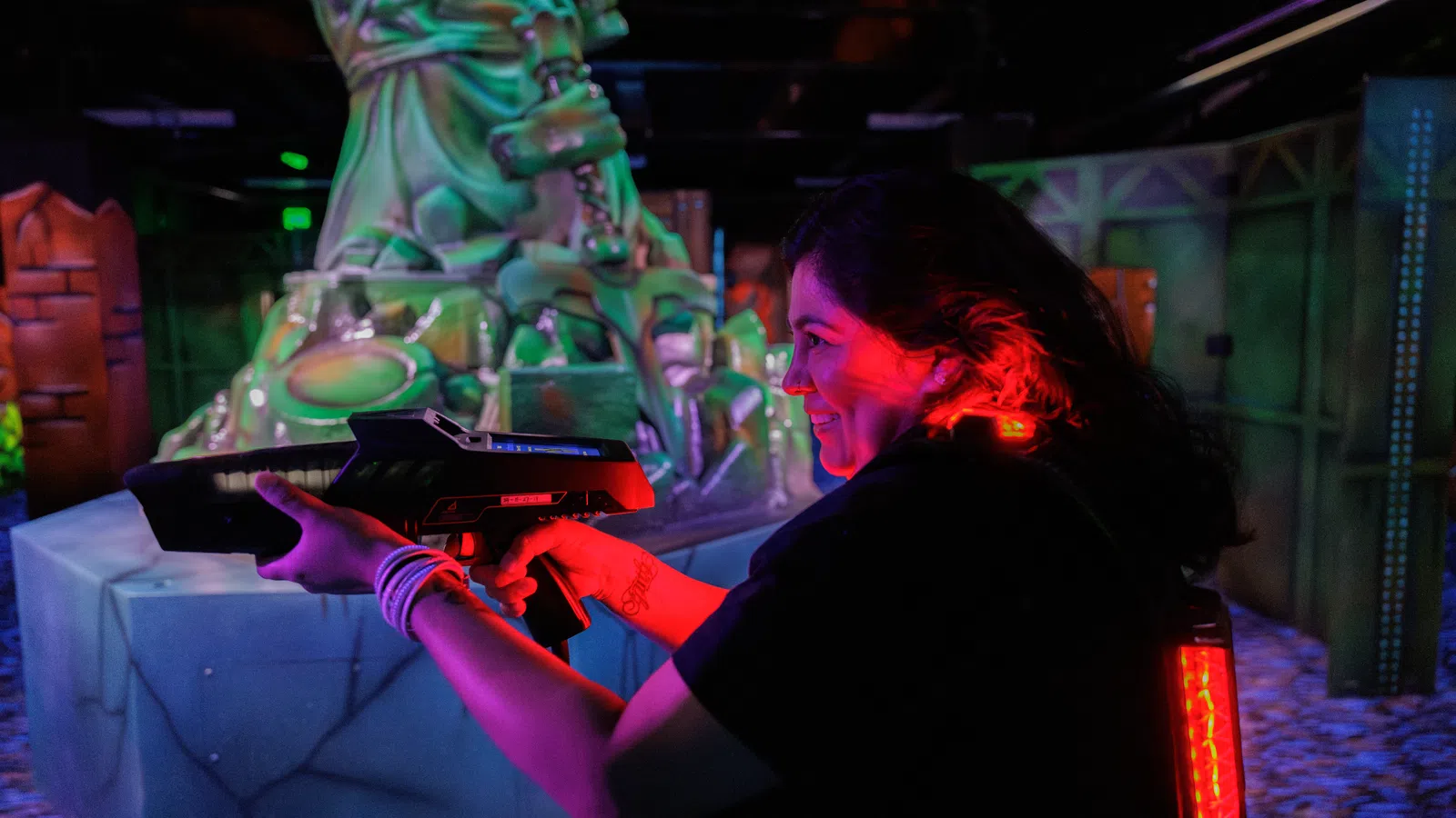 Young woman playing laser tag aiming a gun in a neon-lit indoor arena with futuristic decor.