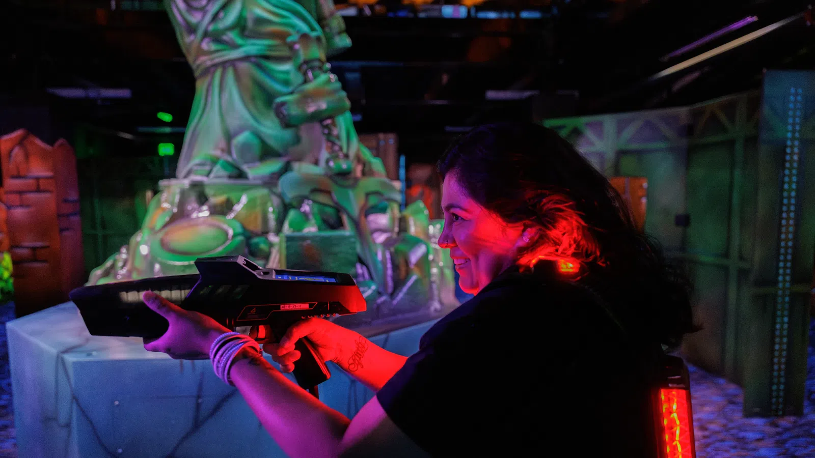 Young woman playing laser tag aiming a gun in a neon-lit indoor arena with futuristic decor.