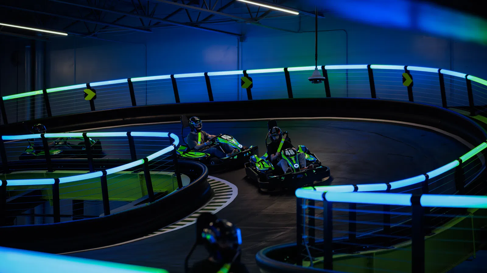 Indoor go-kart racing on a curved track illuminated with vibrant blue and green LED lights under low lighting.