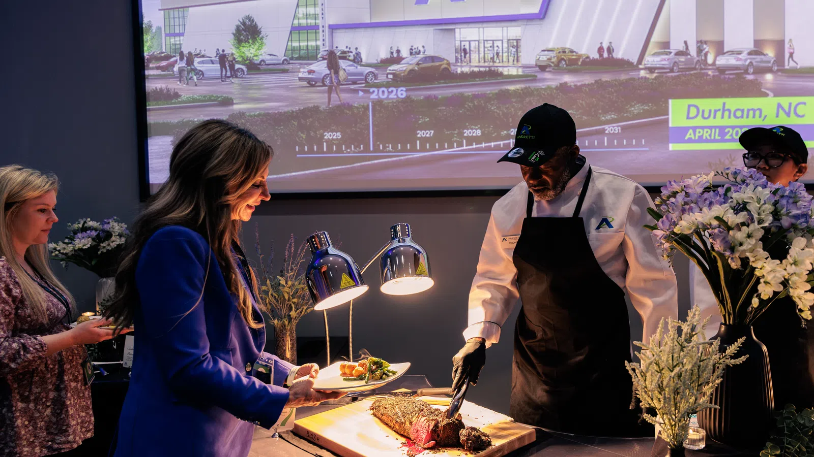 Chef carving roast meat for woman at buffet station during indoor event with digital timeline backdrop.