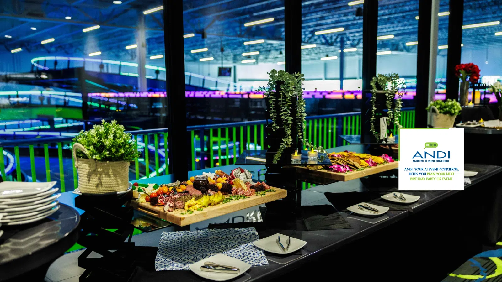 Elegant buffet setup with charcuterie boards, plates, and decorative plants overlooking an indoor sports arena.