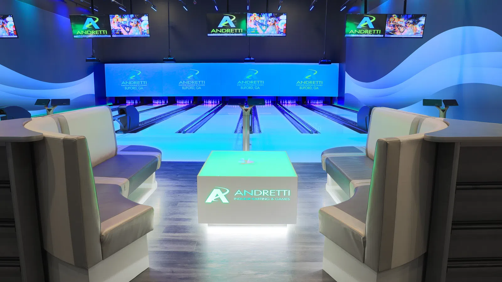 Modern bowling alley with illuminated lanes, comfy seating, and Andretti Entertainment branding on screens and table.