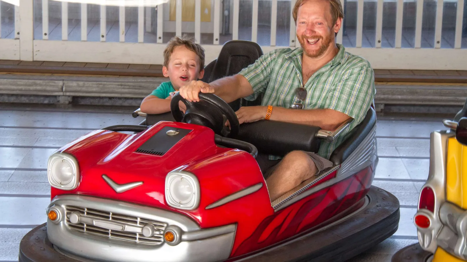 Father and son enjoying a ride in a red bumper car at an indoor amusement park.