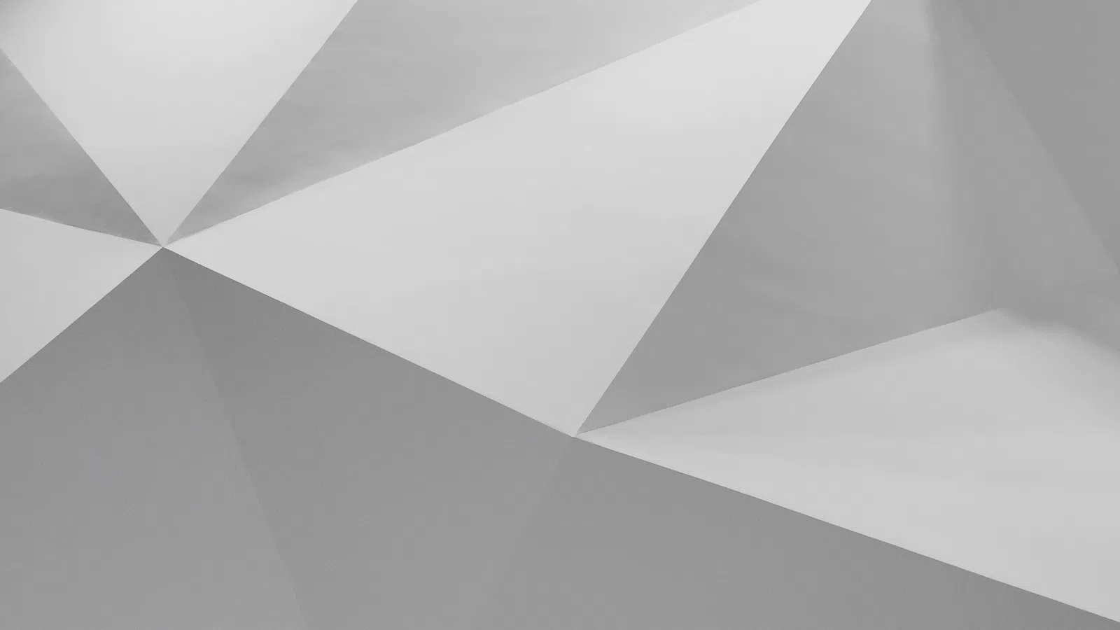 Abstract geometric background with intersecting white and gray triangular facets and sharp edges.