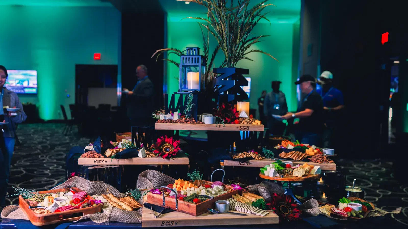 Elegant buffet table with assorted cheeses, crackers, fruits, and decorative candles in event setting.