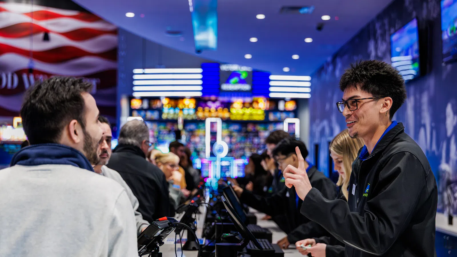 Customers interacting with friendly staff across a bright, busy casino or entertainment venue counter with digital screens.