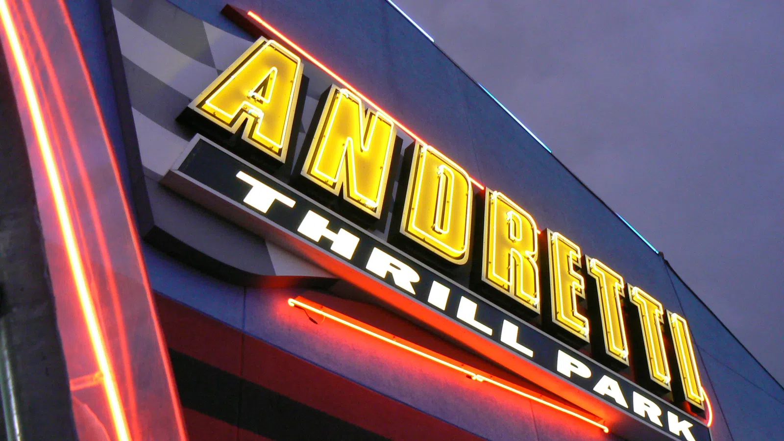Bright yellow ANDRETTI neon sign with THRILL PARK in white below glowing against a dusky sky