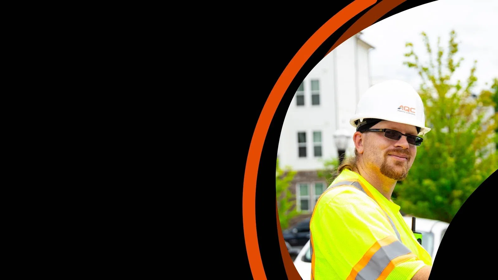 Construction worker in safety gear and helmet smiling outdoors near residential buildings.