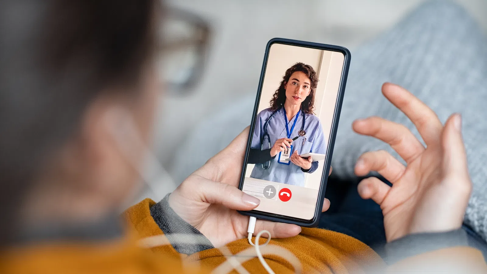 Person holding smartphone having a video call with a female doctor in medical scrubs showing a tablet screen.