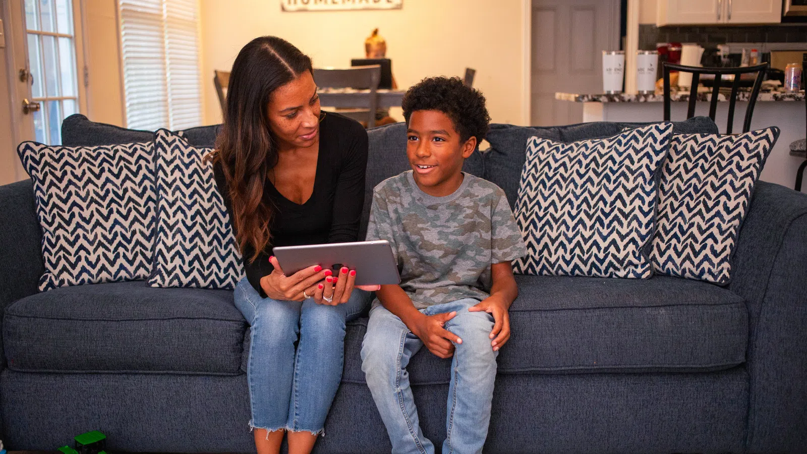a person and a boy sitting on a couch looking at a laptop