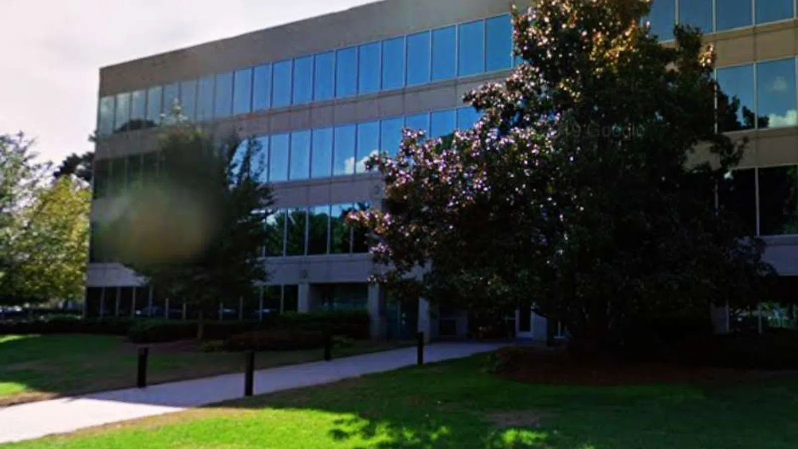 Modern glass office building with reflective windows, surrounded by trees and a well-maintained lawn on a sunny day