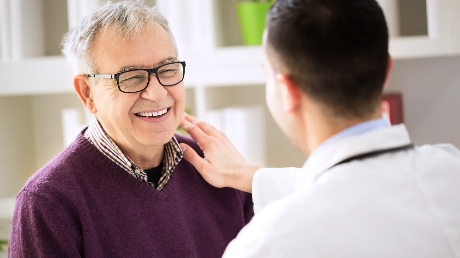 Smiling elderly man wearing glasses talks with doctor in white coat during medical consultation