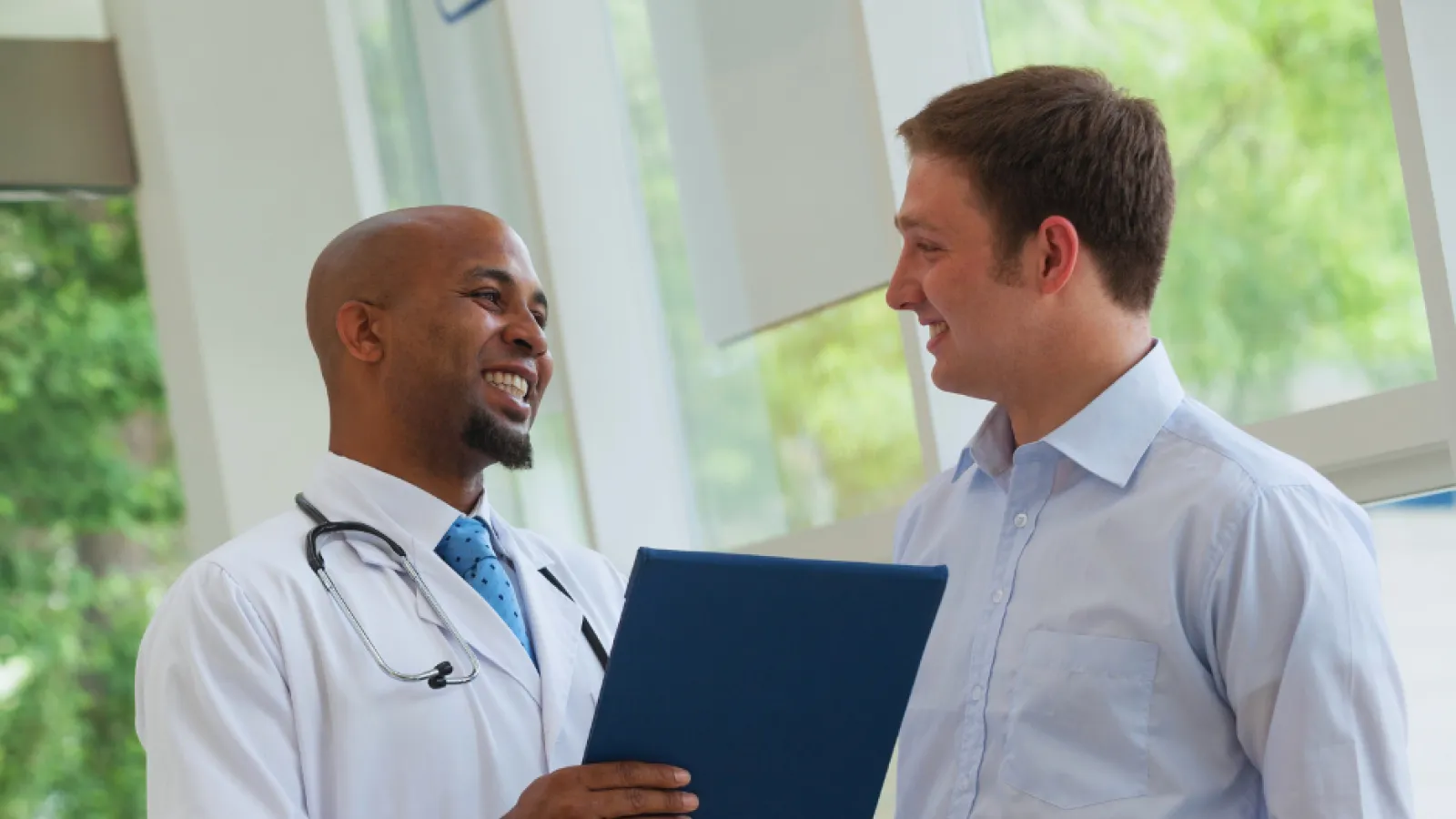 Doctor in white coat consulting and smiling with male patient in bright modern clinic environment