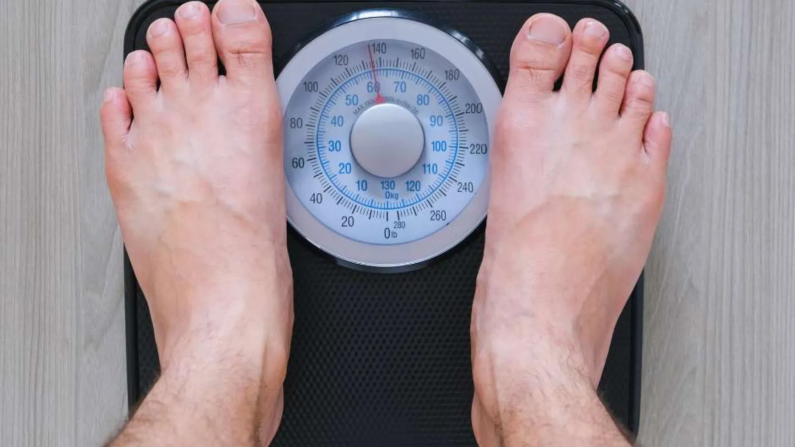 Close-up of feet on a mechanical bathroom scale showing a weight measurement around 145 pounds.