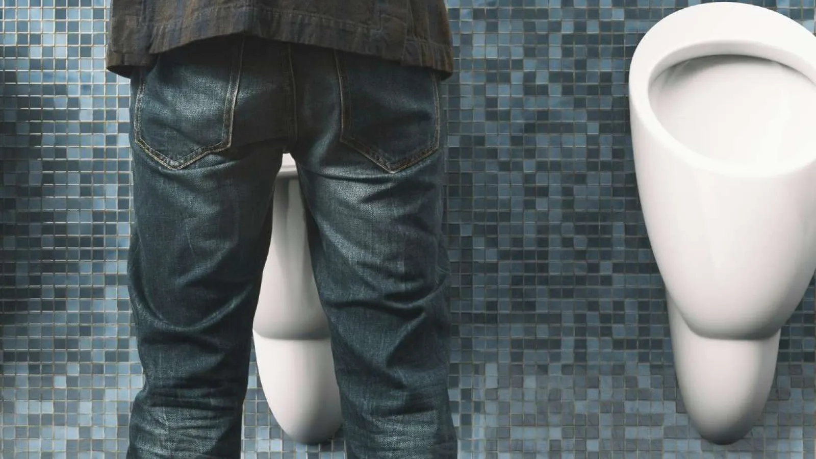 Man wearing jeans standing at a urinal in a public restroom with blue mosaic tiled walls.