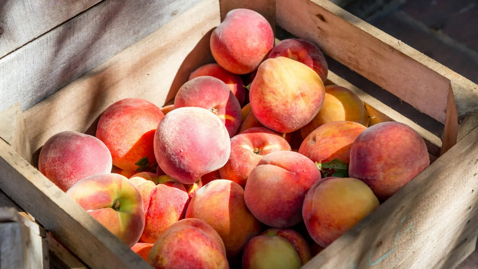 A wooden crate filled with fresh, ripe peaches basking in sunlight.