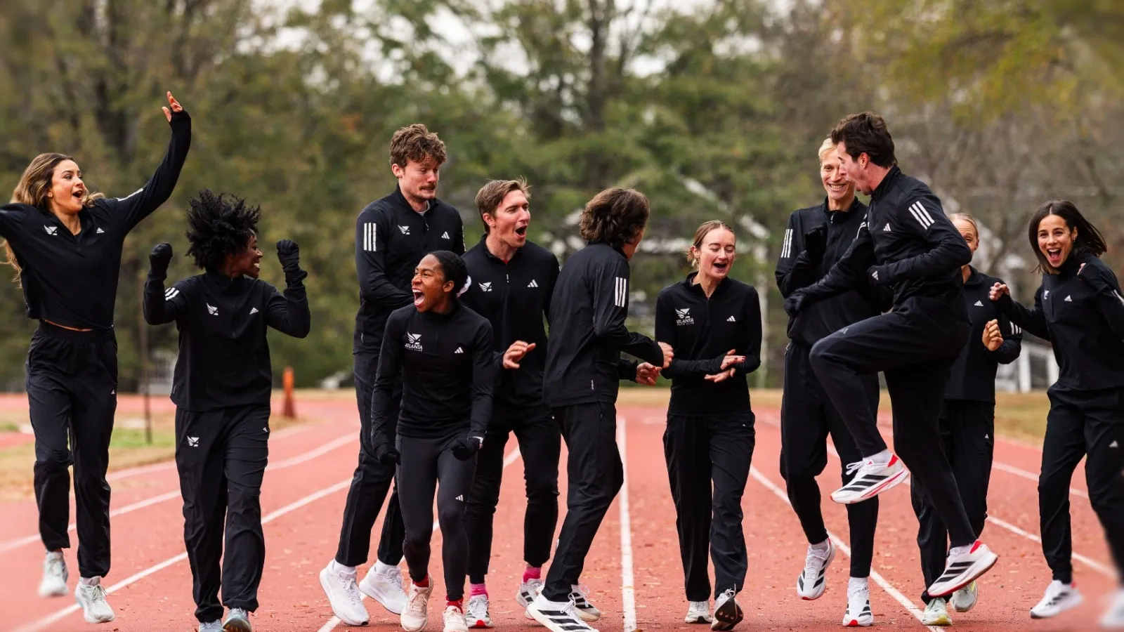 Group of diverse athletes in black tracksuits celebrating on an outdoor running track with trees in background