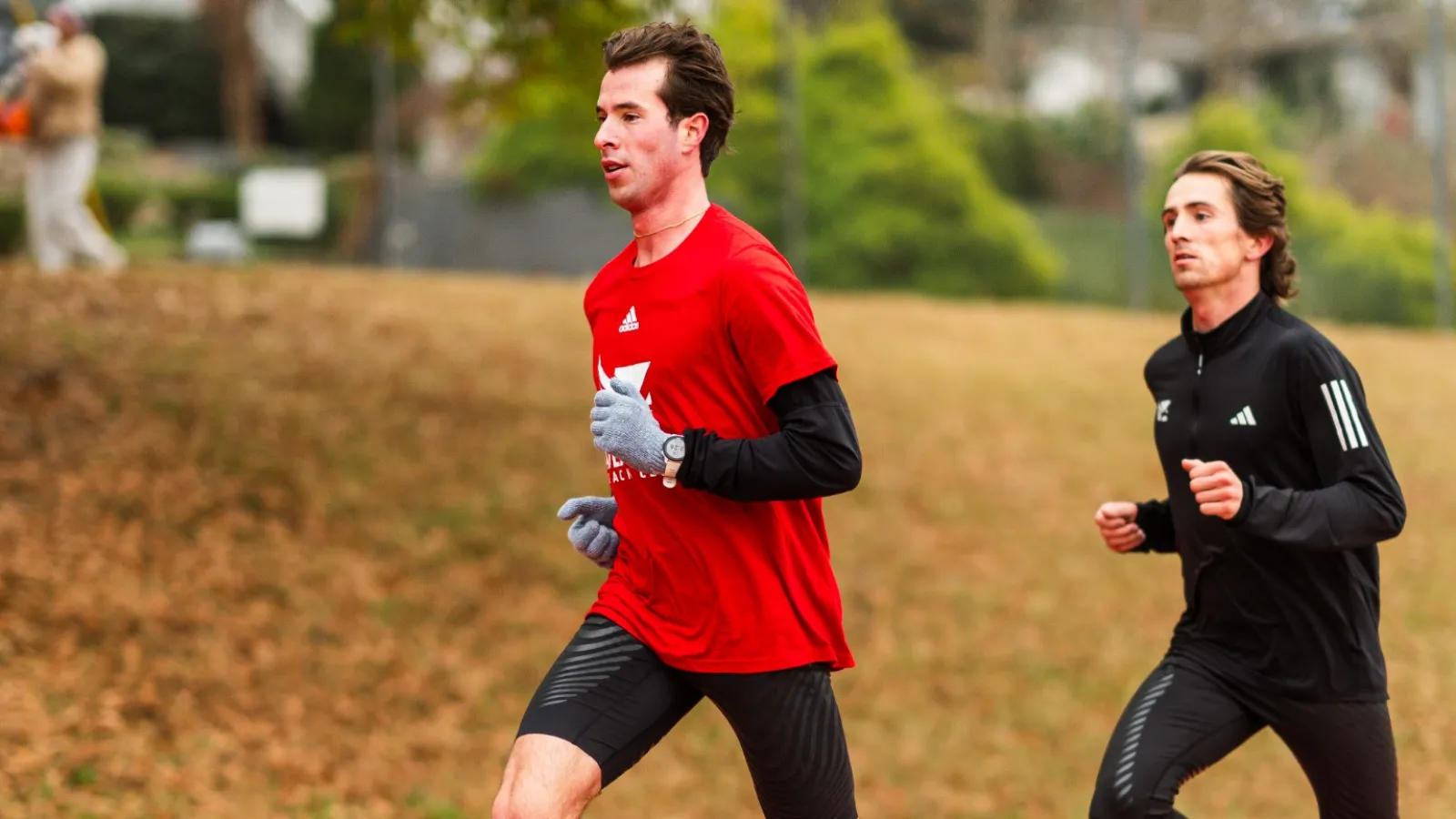Two male runners training on an outdoor track, wearing athletic gear in red and black during daytime.