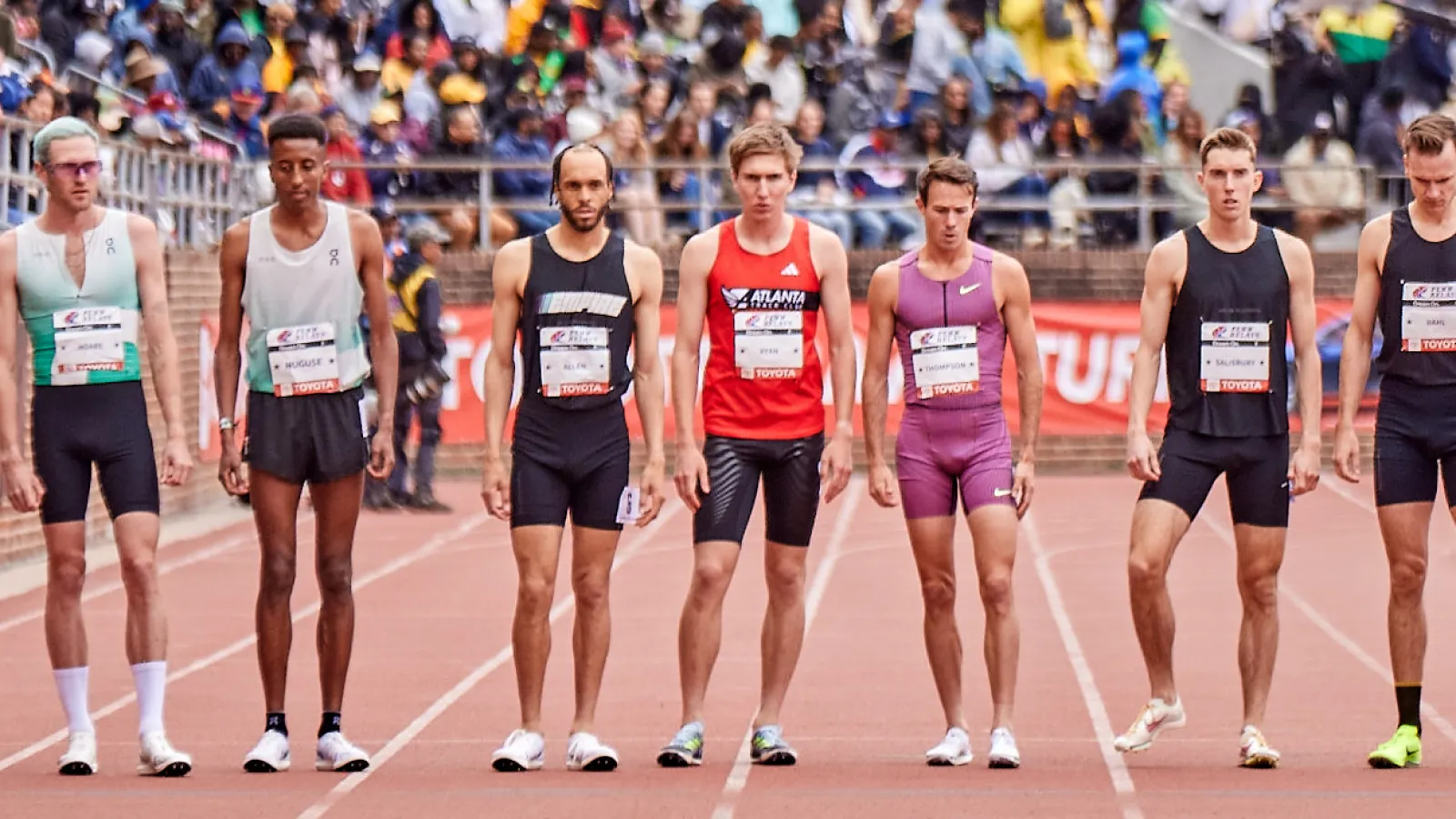 a group of people running on a track with a crowd watching