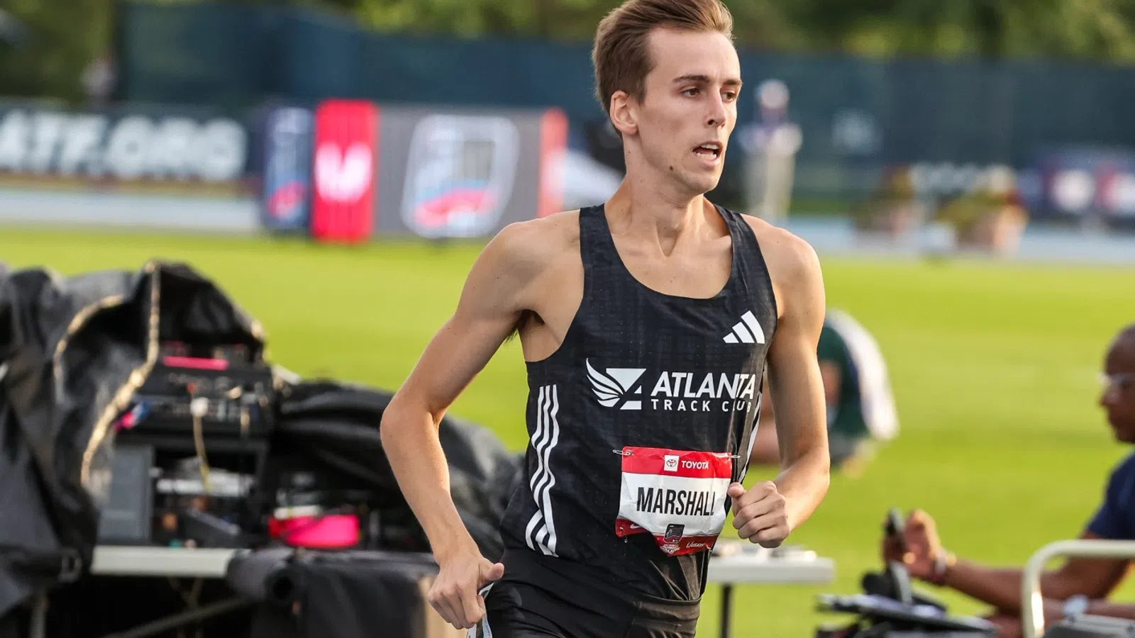 Male athlete in black Atlanta Track Club uniform running on track during a competition at an outdoor event
